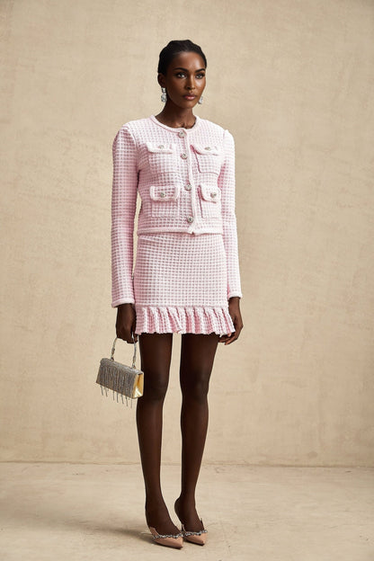 A pink waffle knit matching set consisting of a jacket and skirt called Fabienne The outfit has a textured pattern and is designed to be worn together as a coordinated ensemble