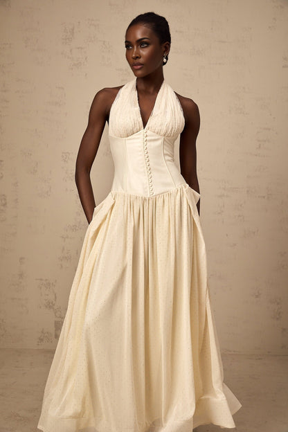 A woman wearing a light blue halter neck tulle midi dress with a fitted bodice and flowy skirt standing against a plain background