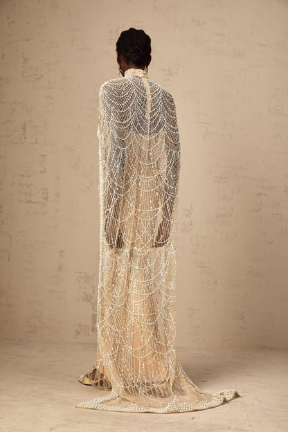 Woman wearing a champagne colored gown with matching beaded cape set named Frederica