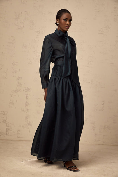 Woman wearing dark green matching shirt and skirt set with ribbon tie neck detail