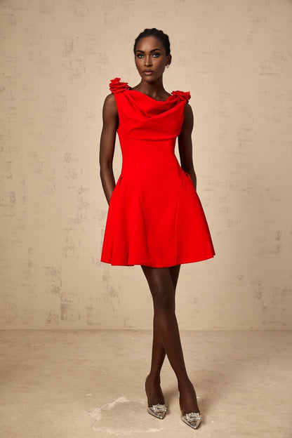 A woman wearing a sleeveless red mini dress with faux flower details standing against a plain background