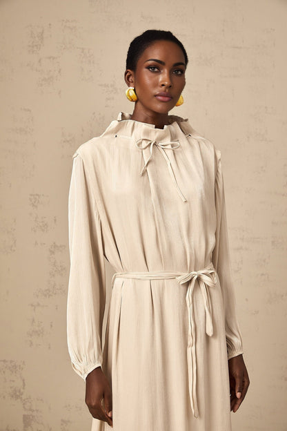 A woman wearing a lightcolored tulle midi dress with a selftie waist standing in a neutral background