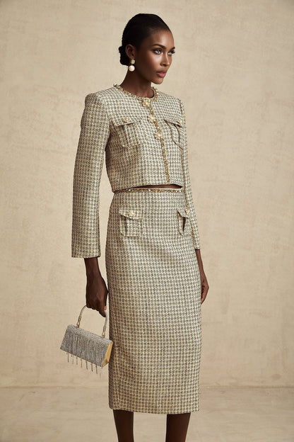 Woman wearing gold tweed sequin jacket and matching skirt set by Aelle standing against plain background
