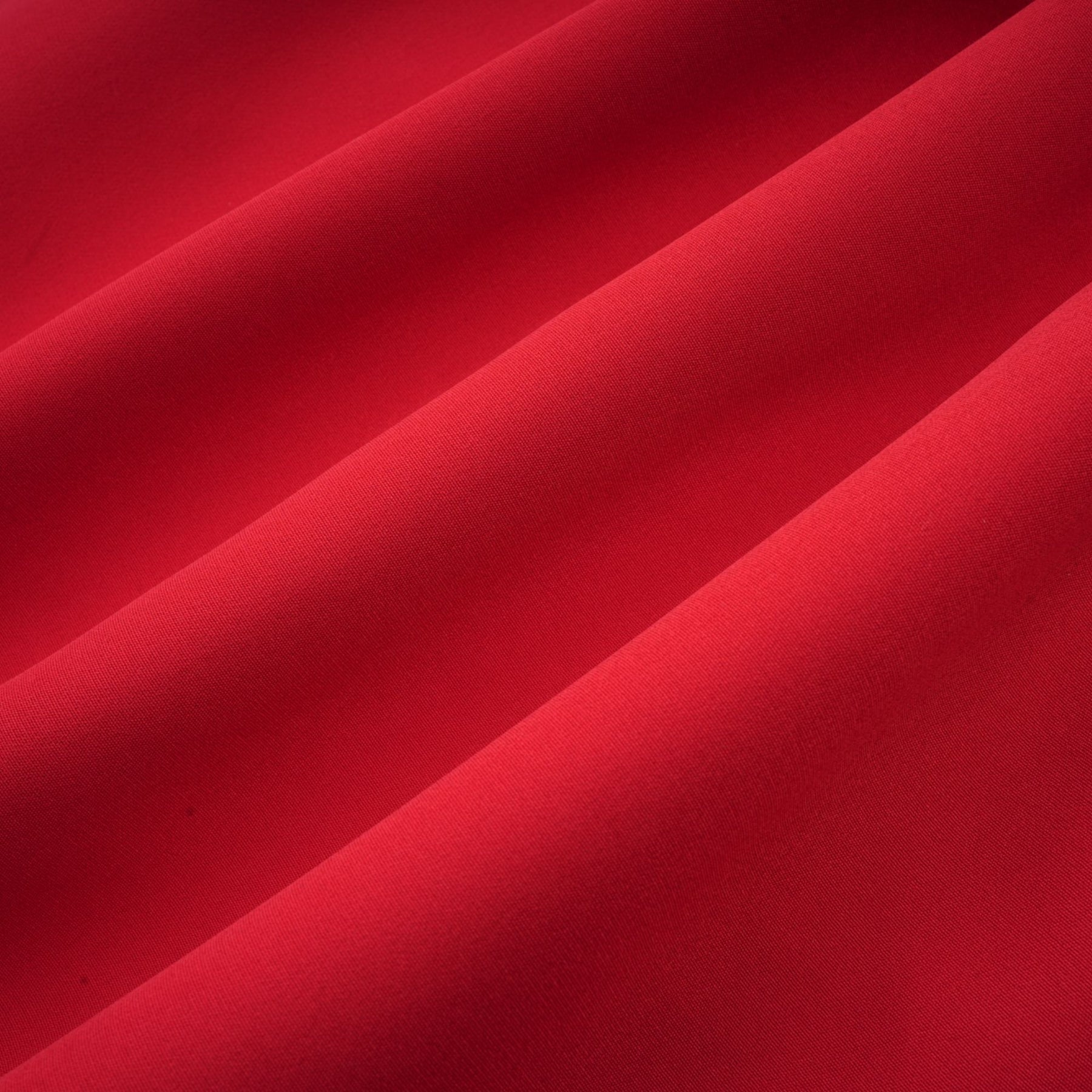 Young woman wearing a short red dress with pleated skirt and embellished details standing against plain background
