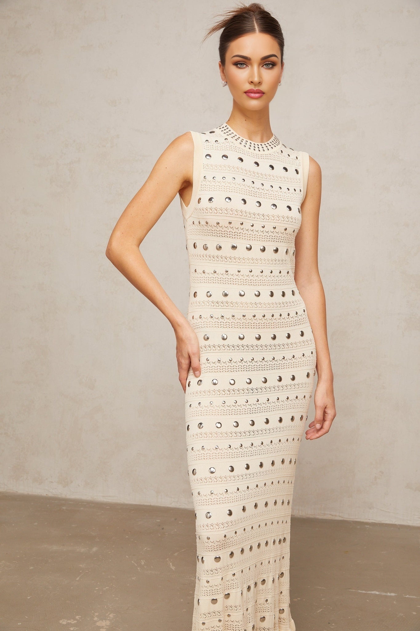 A long neutralcolored maxi dress with crochetknit pattern and studded details designed by Chloé