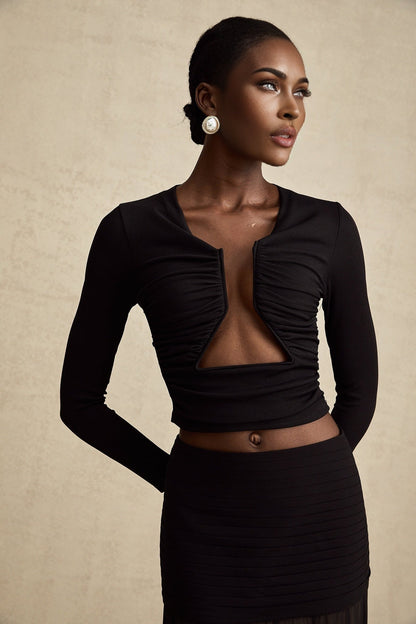 A black sleeveless top with an open front design and gathered fabric details worn by a model
