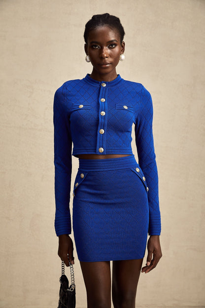 Young woman wearing a blue knitted two piece outfit consisting of a long sleeve top with button details and a matching skirt