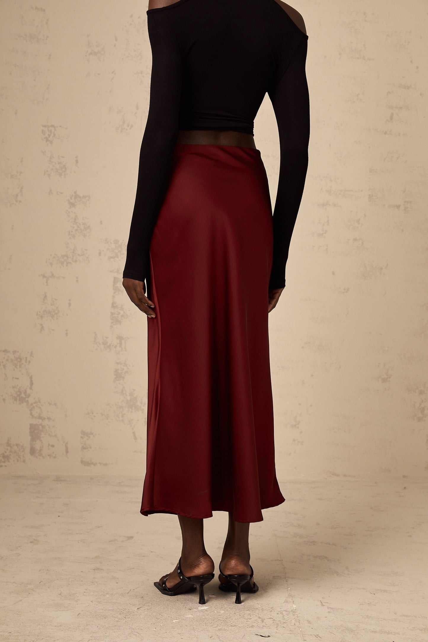Woman wearing bright red satin skirt with flared silhouette against plain background