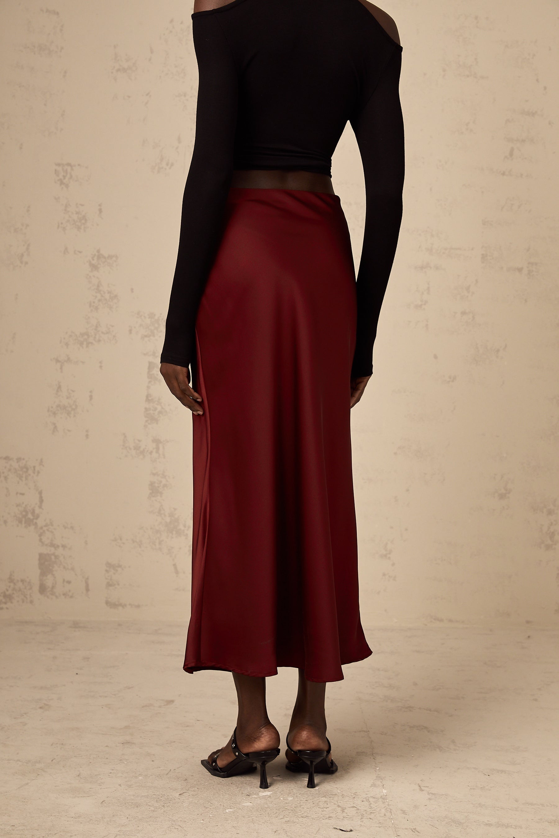Woman wearing bright red satin skirt with flared silhouette against plain background