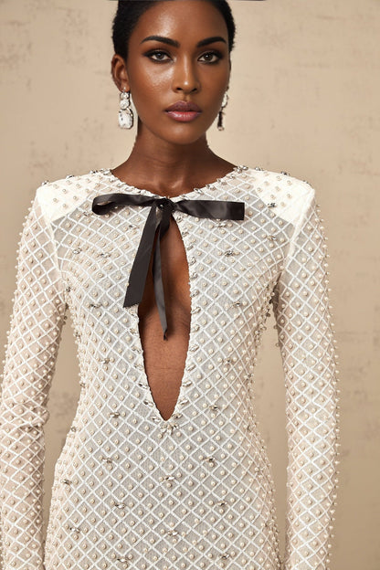 Young woman wearing white mini dress with cutout details and bowknot embellishment standing against plain background