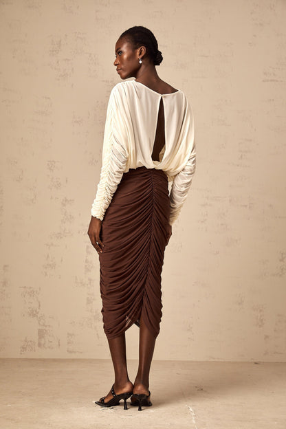 A woman wearing a midi length dress with color blocking and ruching The dress features a prominent flower brooch accent and combines multiple colors in its design