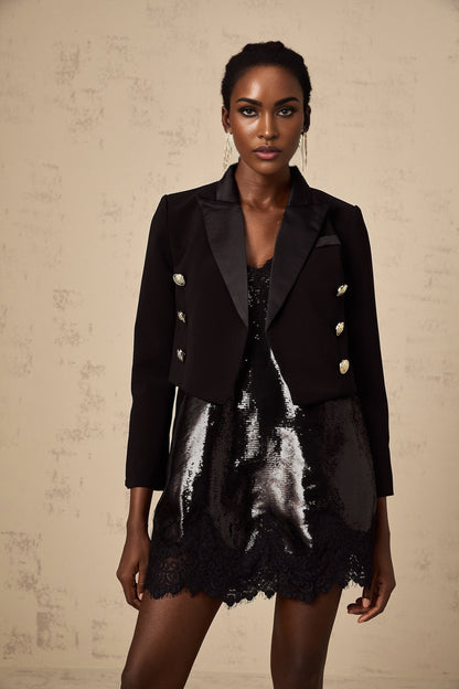 A black cropped blazer with double breasted design worn by a model against a plain background