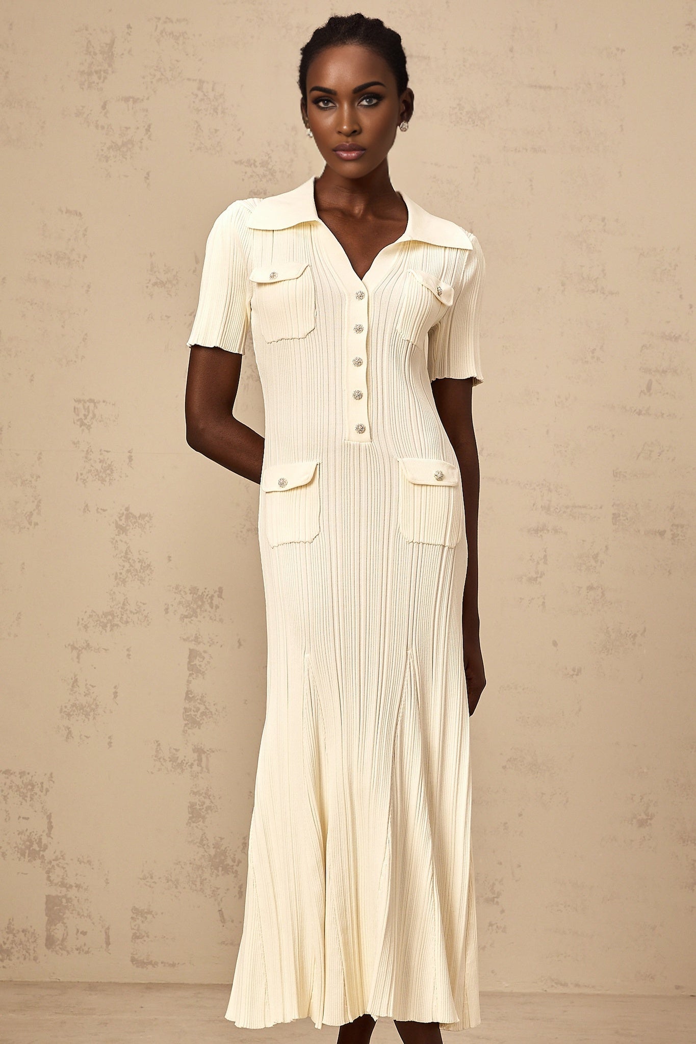 A woman wearing a neutralcolored ribbed knit midi dress with long sleeves standing against a plain background