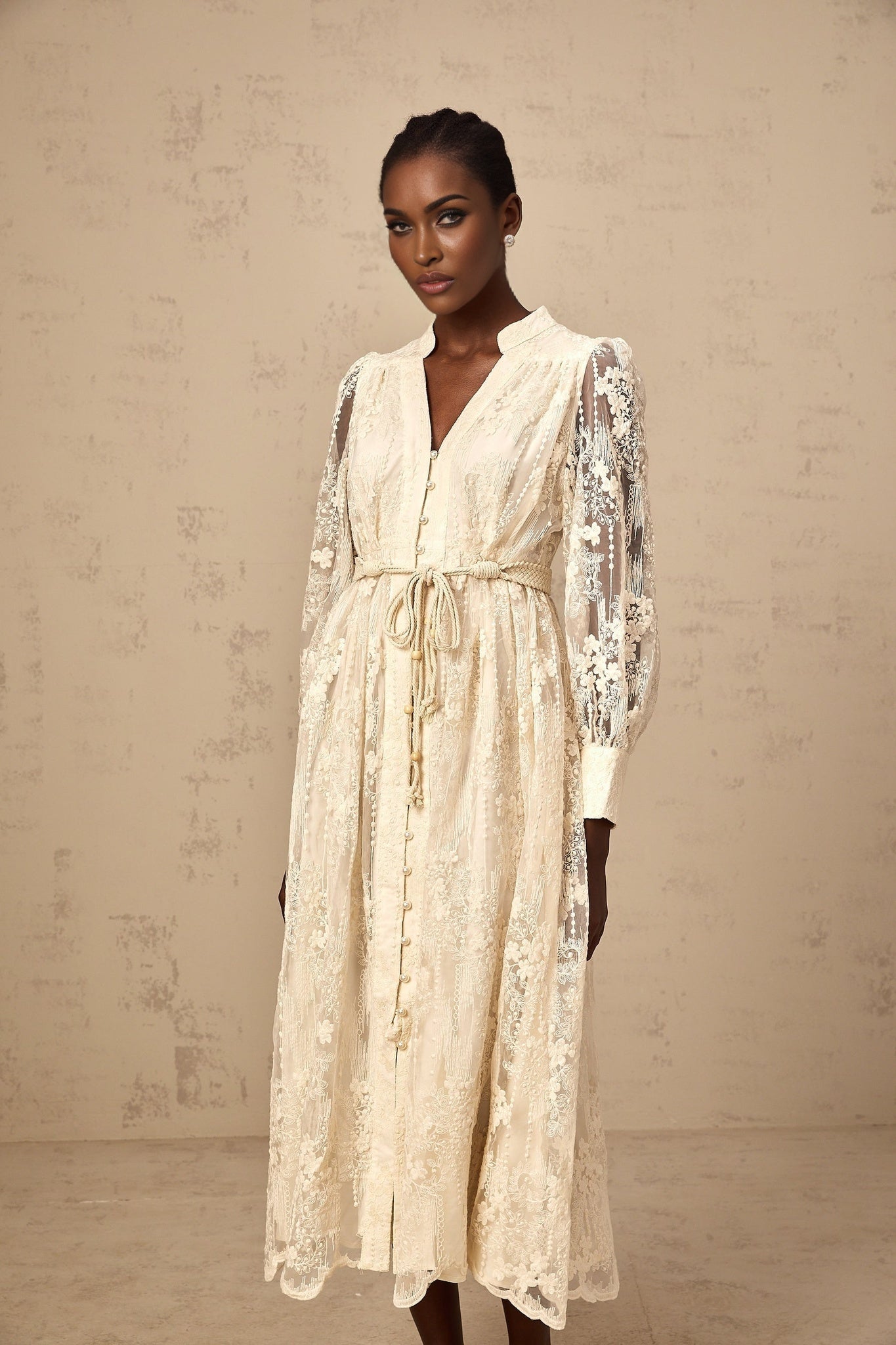 Woman wearing a beige midi dress with lace embroidery details standing in a neutral background