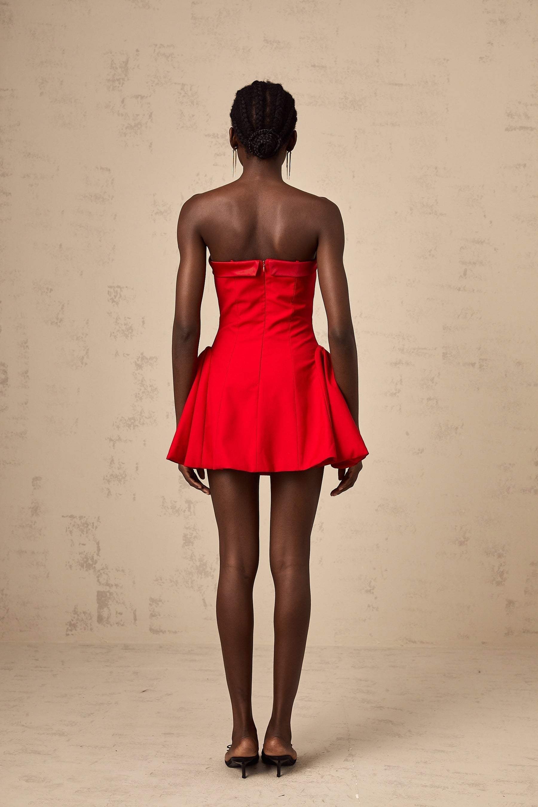A woman wearing a red offshoulder mini dress with flared sleeves and a short skirt posing against a plain background