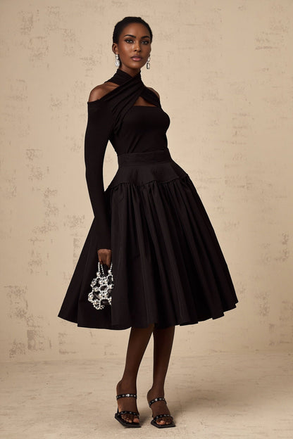 Woman wearing a black pleated midi skirt with flared silhouette standing against a plain background