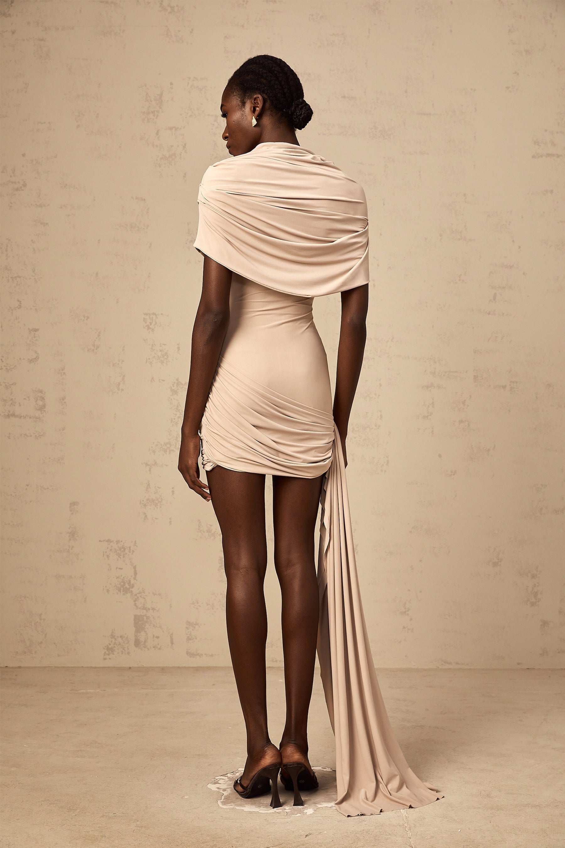 A woman wearing a beige mini dress with capelike sleeves and ruched detailing fitted to the body