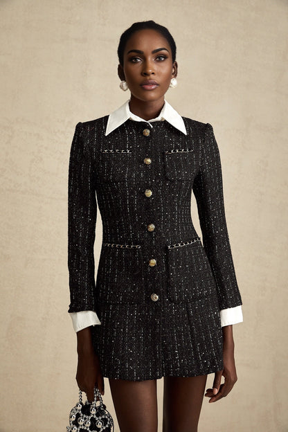 A woman wearing a black mini dress with a tweed fabric base and sequin panels standing against a plain background