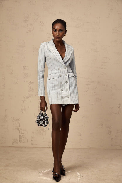 A young woman wearing a light blue denim mini dress with rhinestone embellishments and a blazer style collar and lapels The dress features long sleeves and a fitted silhouette