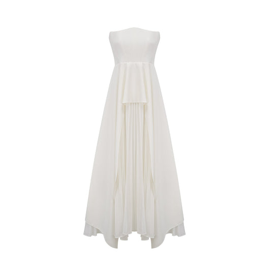A woman wearing a long white pleated maxi dress with an offshoulder neckline