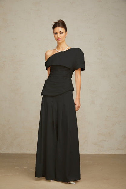 Woman wearing black matching set with creased top and trousers standing against plain background