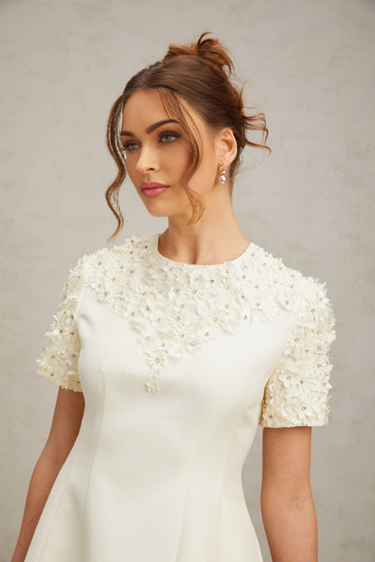 A short white mini dress with colorful floral applique designs scattered across the fabric featuring a sleeveless cut and a fitted silhouette