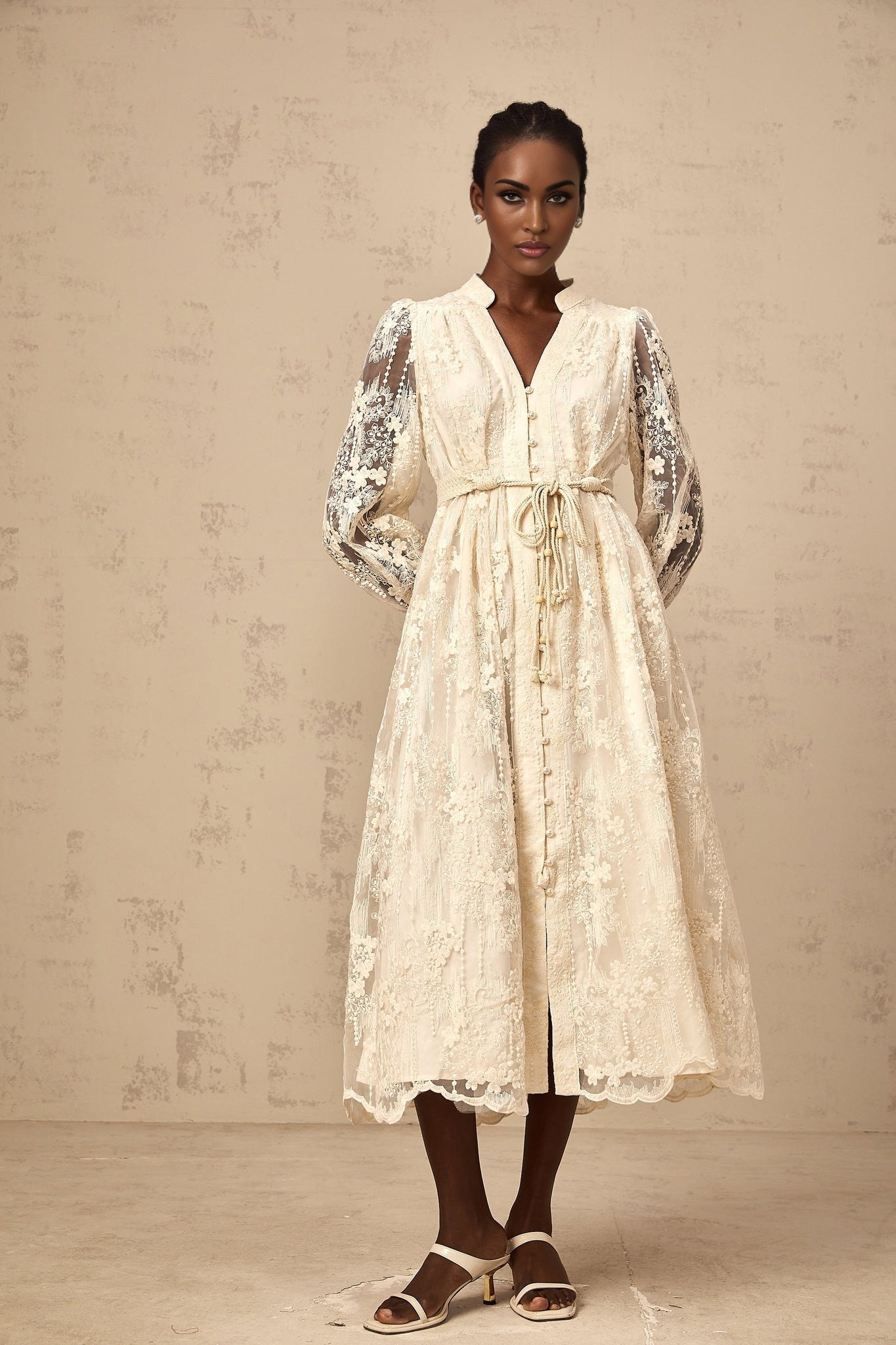 A woman wearing a neutralcolored midi dress with delicate lace embroidery details standing in a casual pose