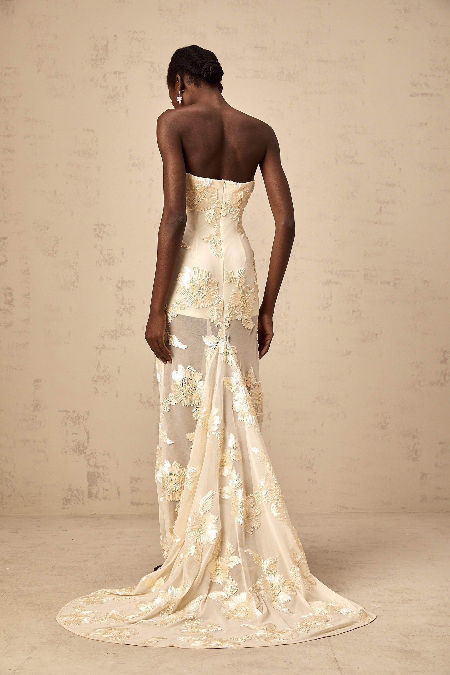 A woman wearing a long offshoulder maxi dress in neutral tones with embroidery details