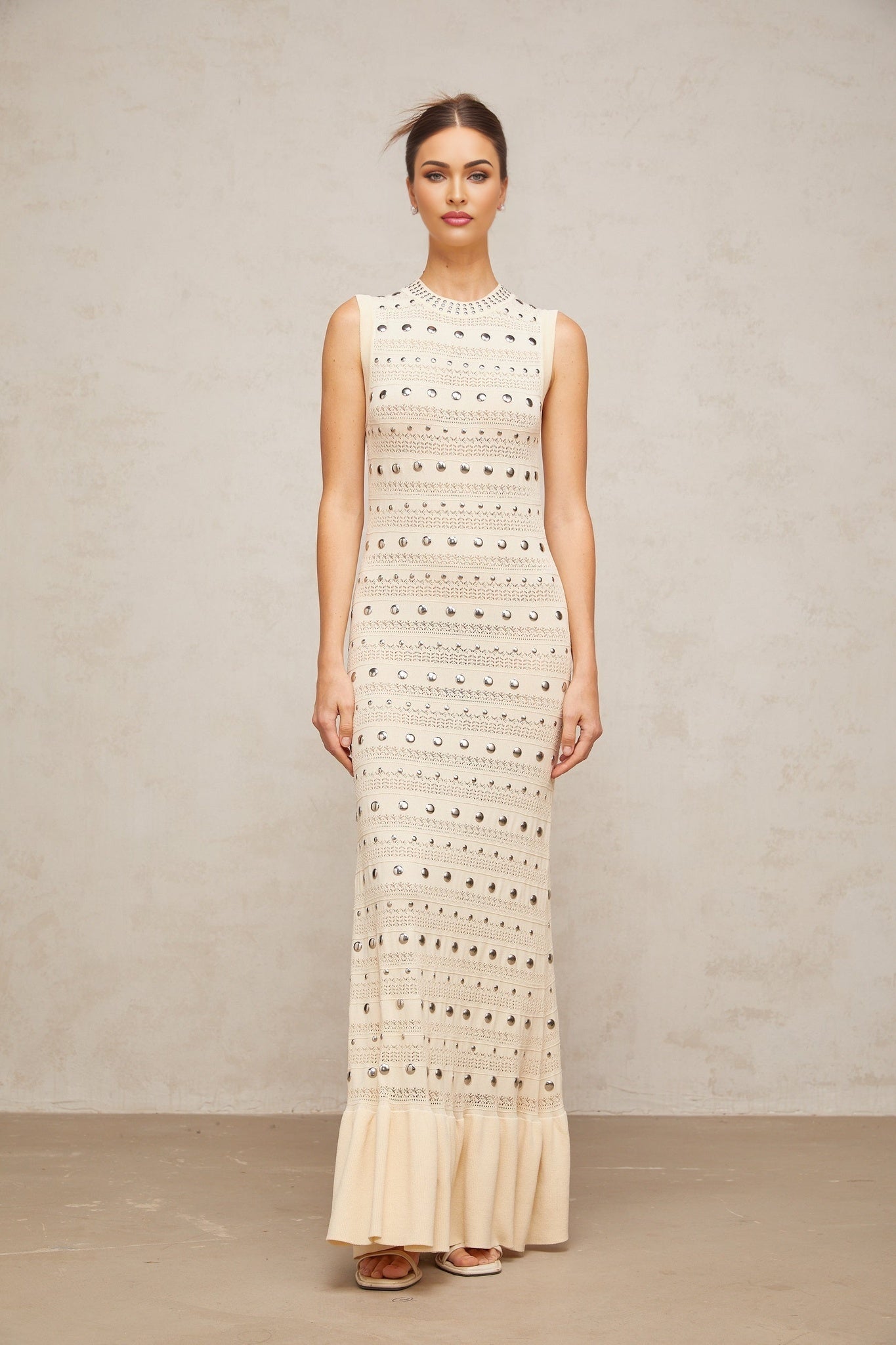 A long neutralcolored maxi dress with crochetknit pattern and studded details made by Chloé