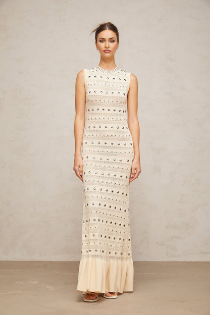 A long neutralcolored maxi dress with crochetknit pattern and studded details made by Chloé