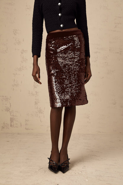 Woman wearing a brown kneelength skirt covered in shimmering sequins standing against a plain background