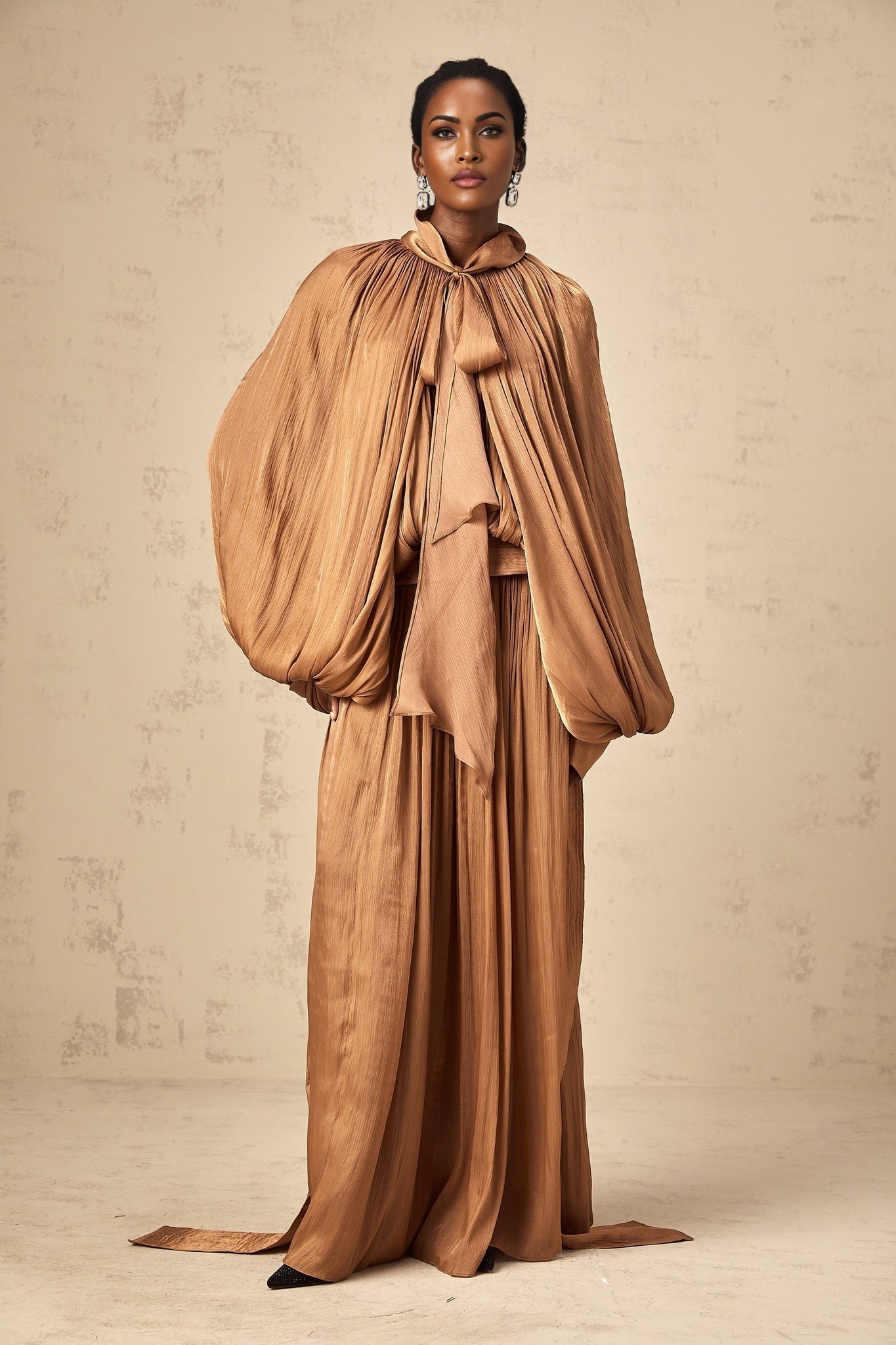 Woman wearing long brown pleated satin maxi dress with flowing skirt and elegant silhouette
