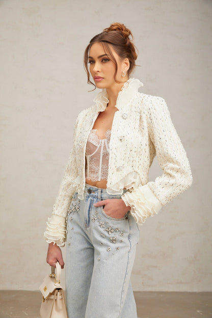 Woman wearing white cropped jacket with beaded embellishments and ruffle details on sleeves and collar