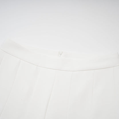 Woman wearing white creased top and matching trousers set standing against plain background