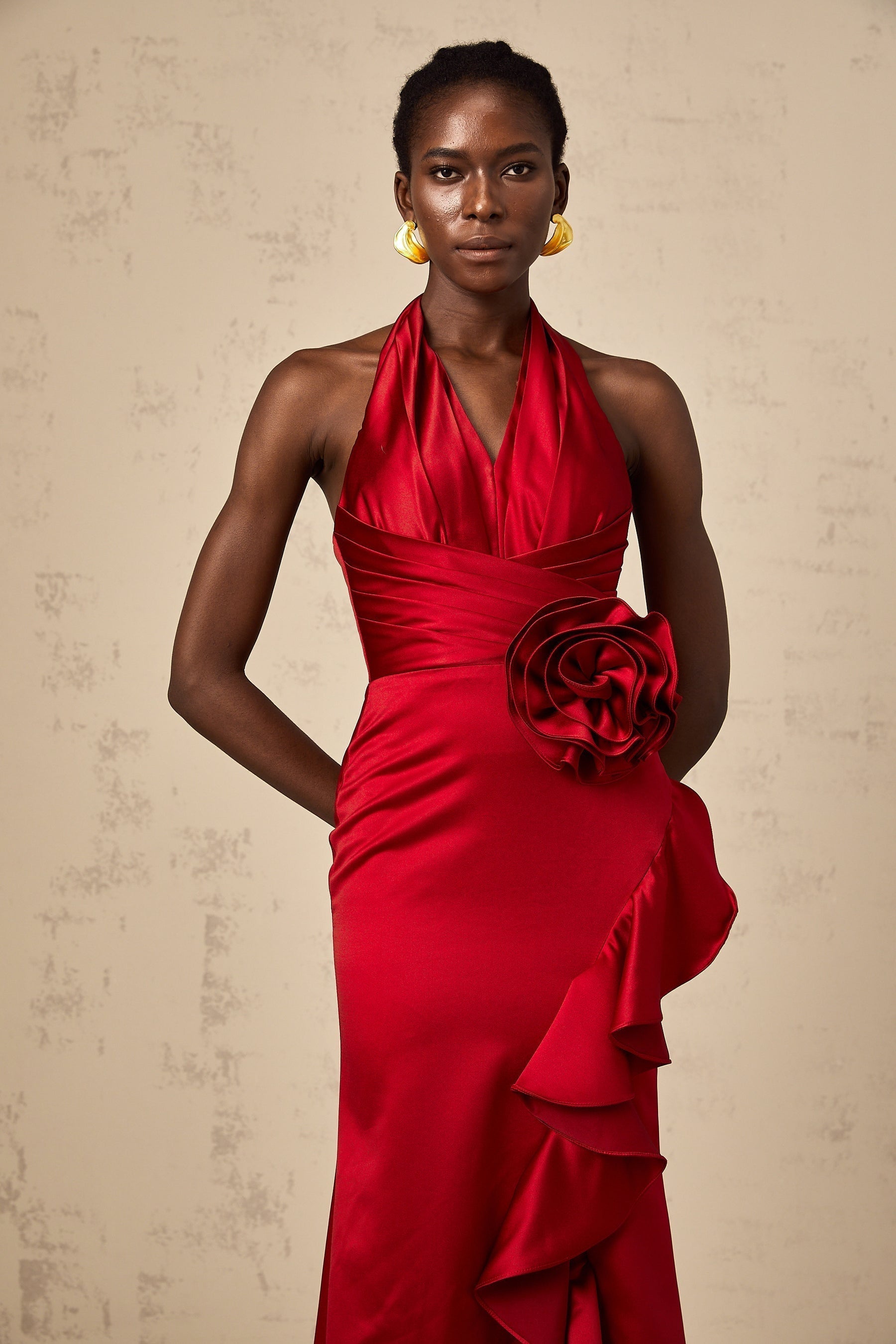 A red halterneck maxi dress with 3D petal ruffles adorning the bodice and skirt featuring a flowing silhouette and open back design