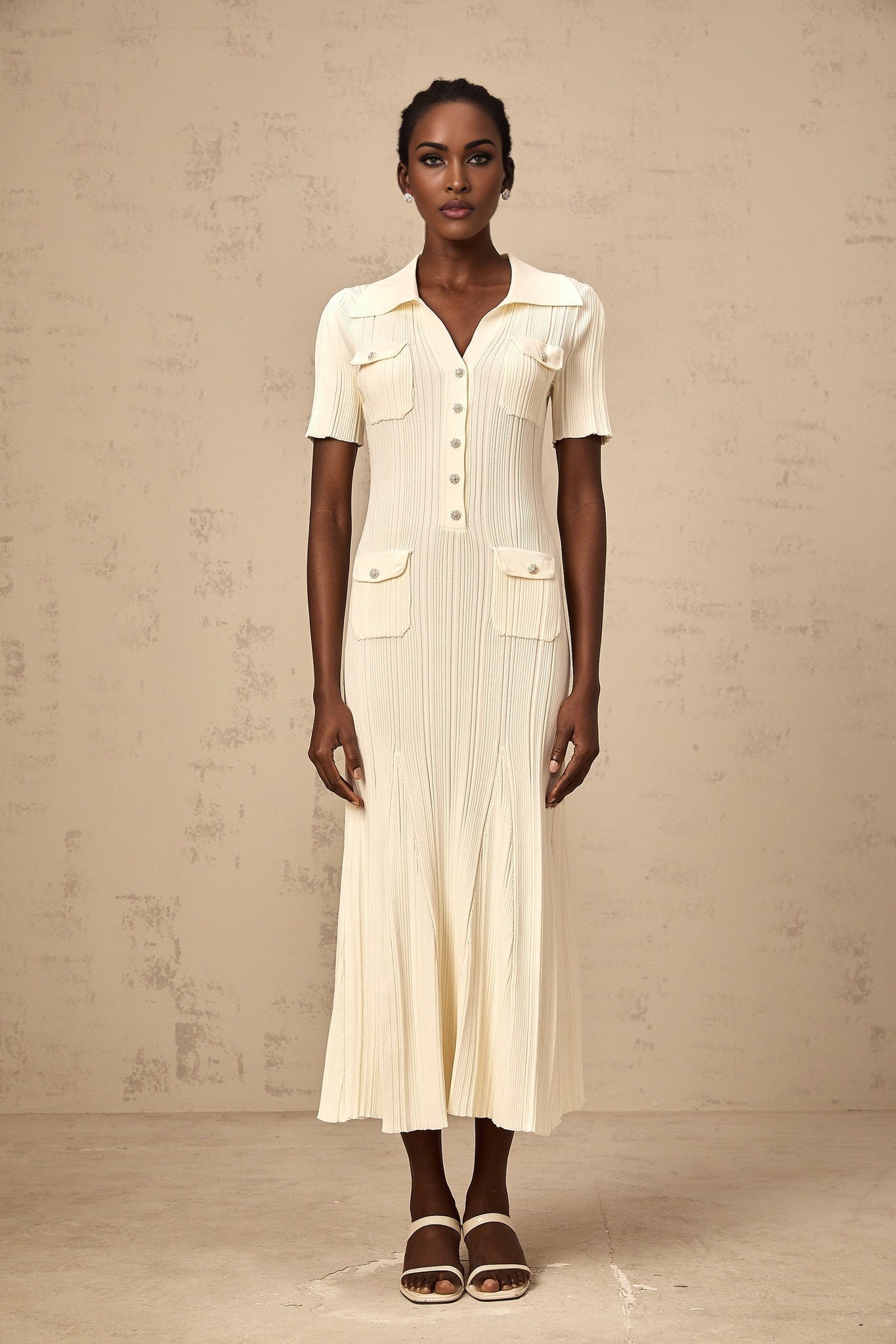 A woman wearing a neutralcolored ribbed knit midi dress with a formfitting silhouette and long sleeves standing in a relaxed pose