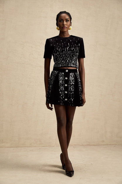 Woman wearing black velvet two piece outfit with embellished top and matching skirt