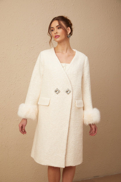 A white collarless coat made of textured fur fabric worn by a model standing against a plain background