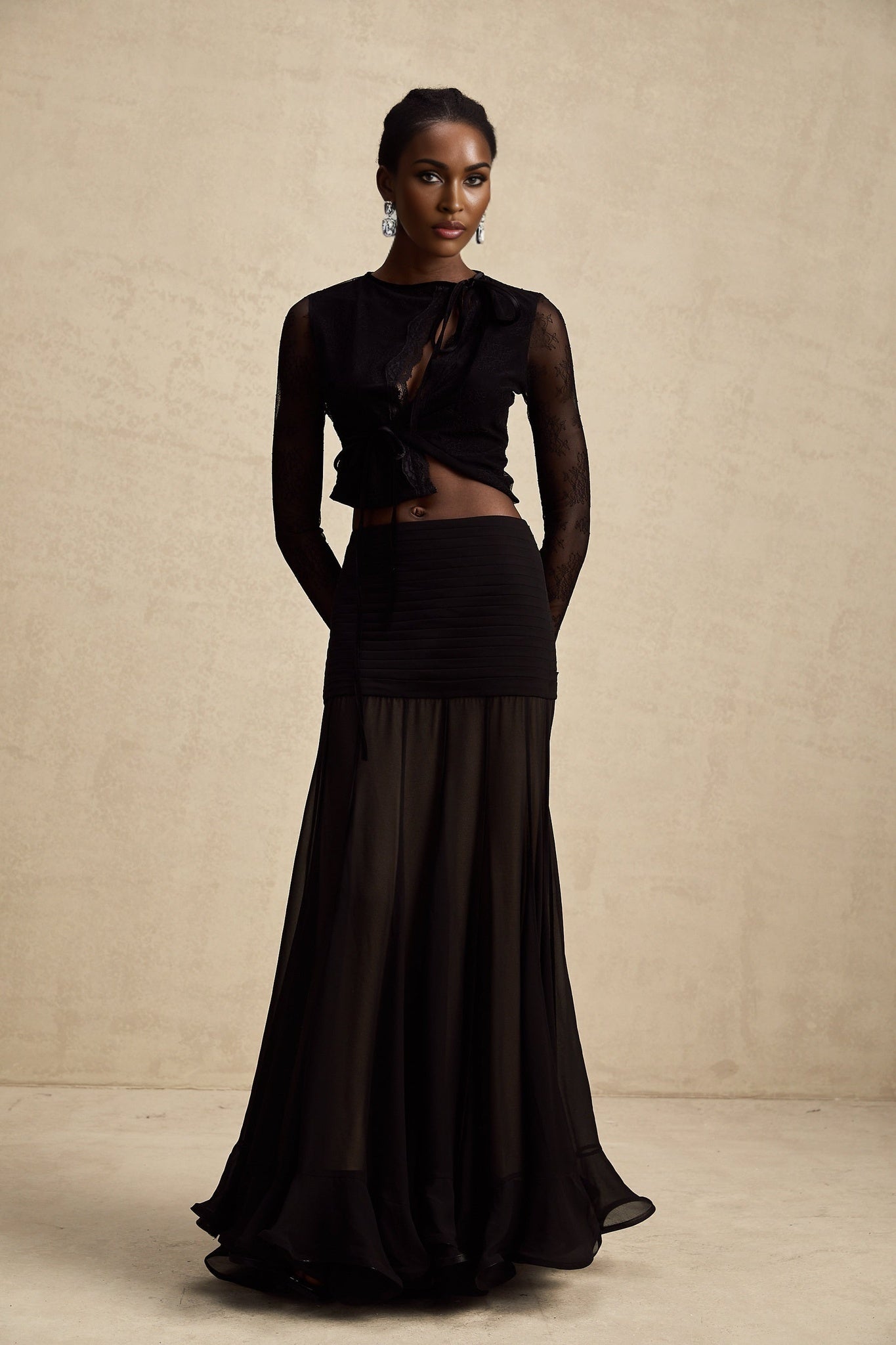 A black cropped top with sheer lace trim and see through details worn by a model against a plain background
