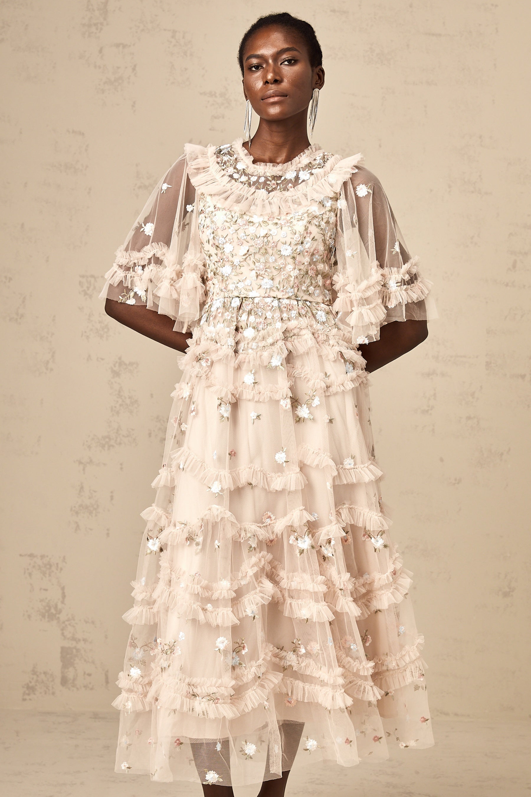A woman wearing a white midi dress with tiered ruffles and floral embroidery standing in a garden setting