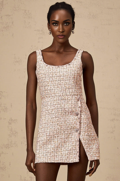 Woman wearing a short pink tweed dress with embellishments and decorative details standing in a neutral background