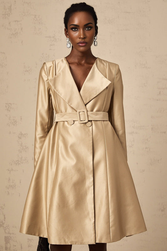 Woman wearing long khaki coat with belt at waist standing in urban setting