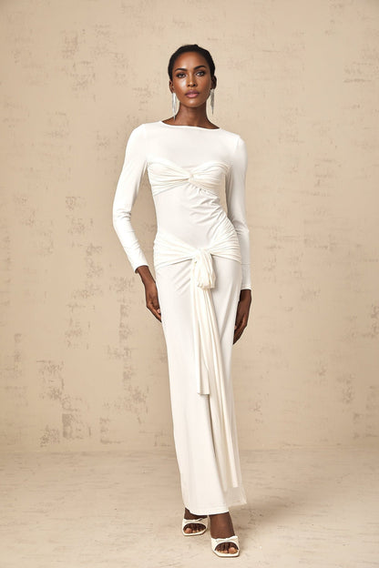 A long white maxi dress with ruched fabric featuring a twist detail and ribbon accents