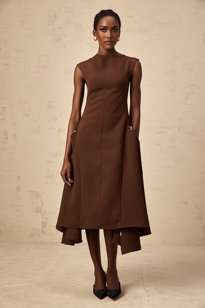 A brown midi dress with an asymmetric design worn by a model standing against a plain background