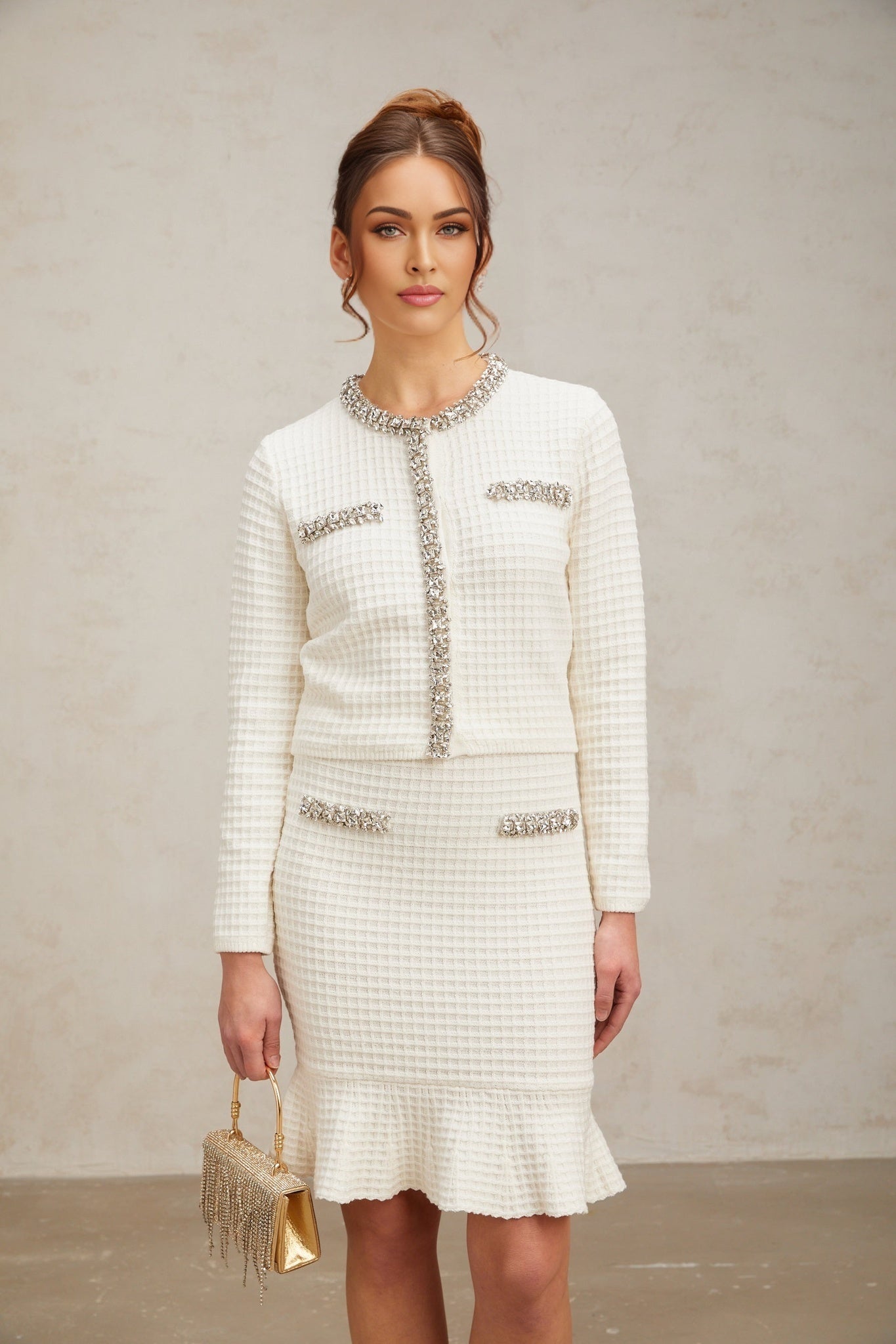 A white waffle knit matching set featuring a cardigan and skirt with embellished details The cardigan has long sleeves and the skirt is knee length Both pieces have a textured waffle pattern and decorative embellishments