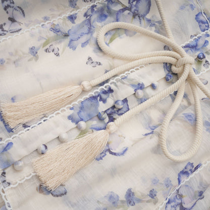 Woman wearing short floral print dress with flared skirt and flowing chiffon fabric in pastel colors against plain background