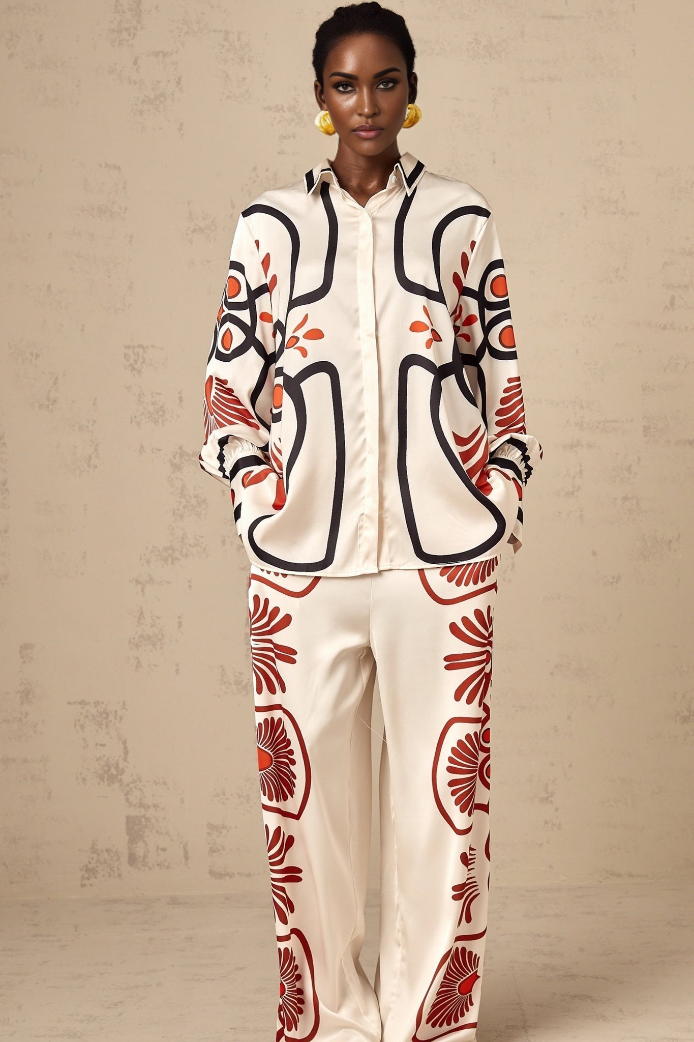 A woman wearing a matching set consisting of a graphicprint shirt and trousers in a bold colorful pattern standing against a plain background