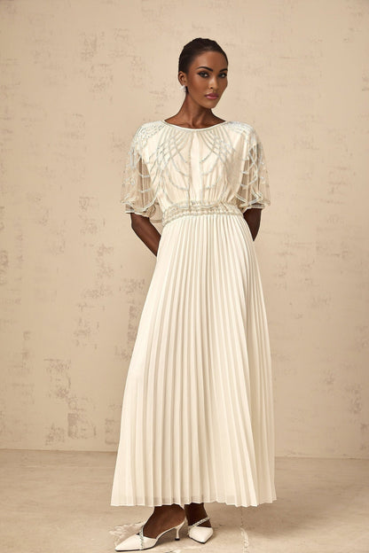 A long white pleated maxi dress adorned with crystal embellishments featuring a flowy silhouette and elegant design