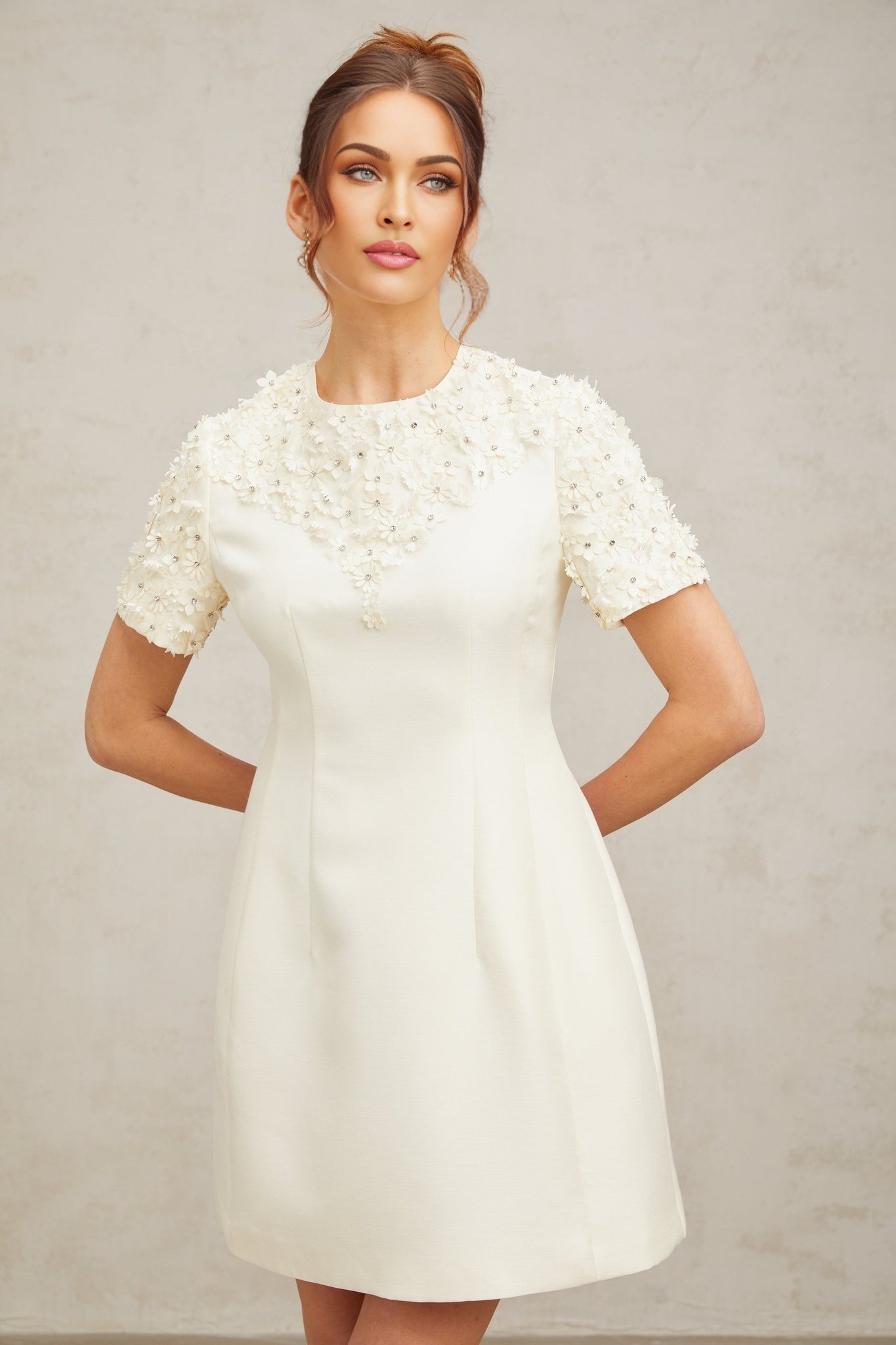 A short white dress with colorful floral appliques scattered across the fabric featuring a fitted bodice and flared skirt