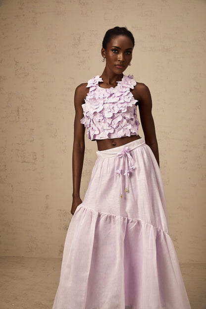 Woman wearing a purple matching set consisting of a sleeveless top and skirt adorned with faux flower details